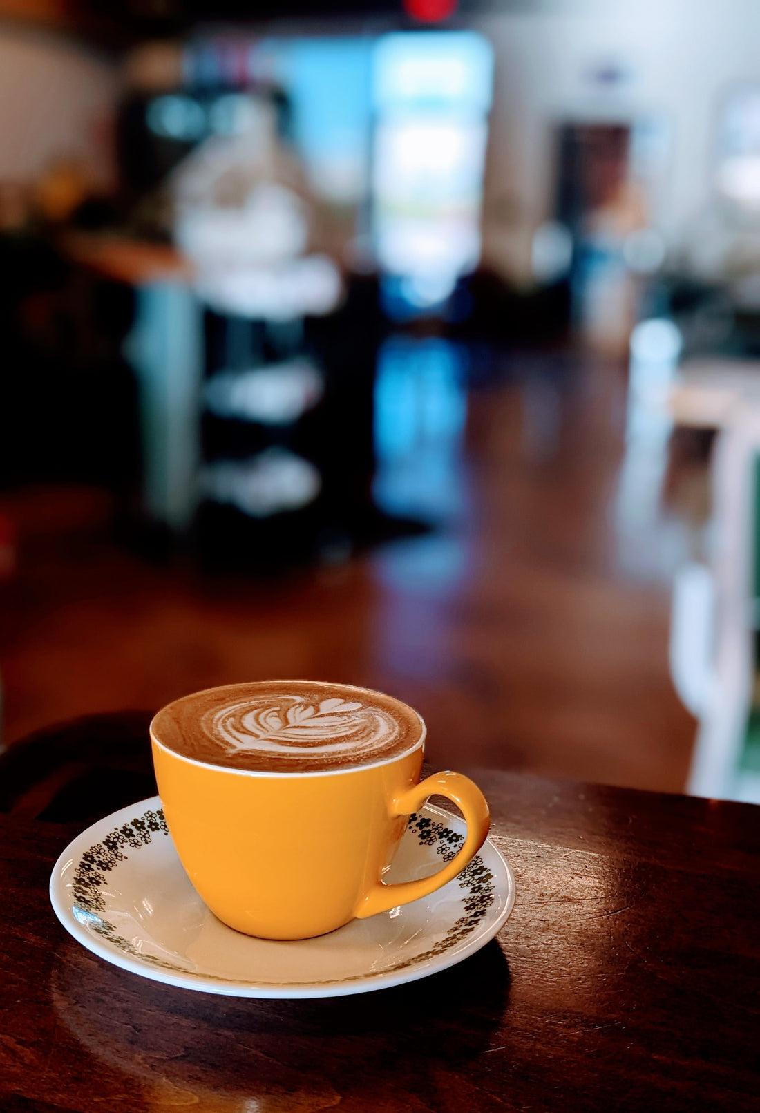 A yellow cup with latte art sitting on a table in a sunlit cafe